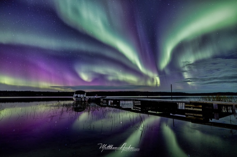 Green and violet aurora over the docks at Cassidy Point, the whole display reflected in still water