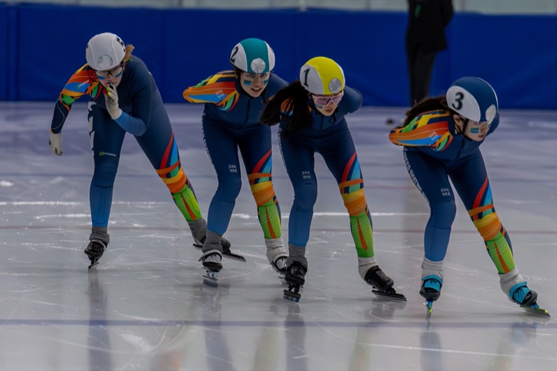 Four short-track speed skaters cornering in a tight line at the Arctic Winter Games