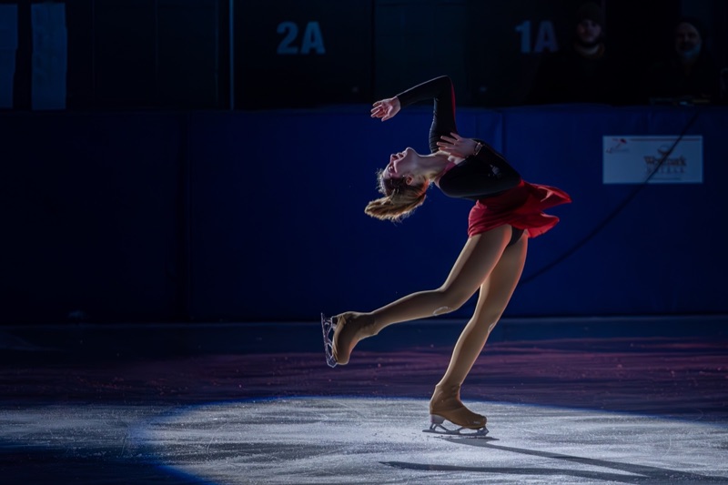 A figure skater arched back mid-spiral under a single spotlight on dark ice