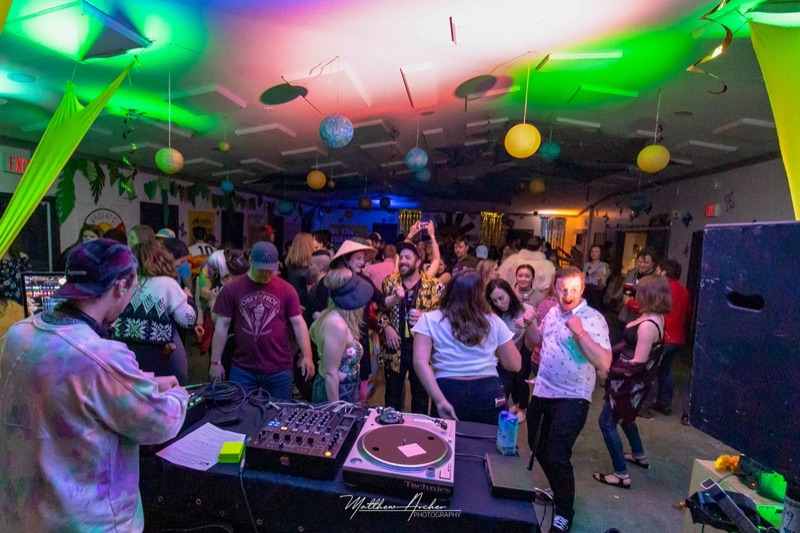 A packed hall dancing under coloured lights and paper lanterns, the DJ working the decks in the foreground