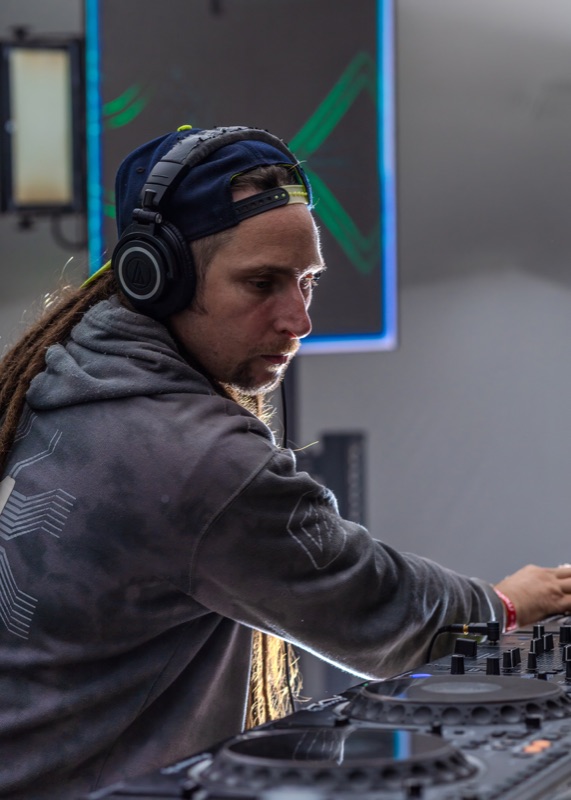 A DJ with long dreadlocks and headphones working the decks in daylight