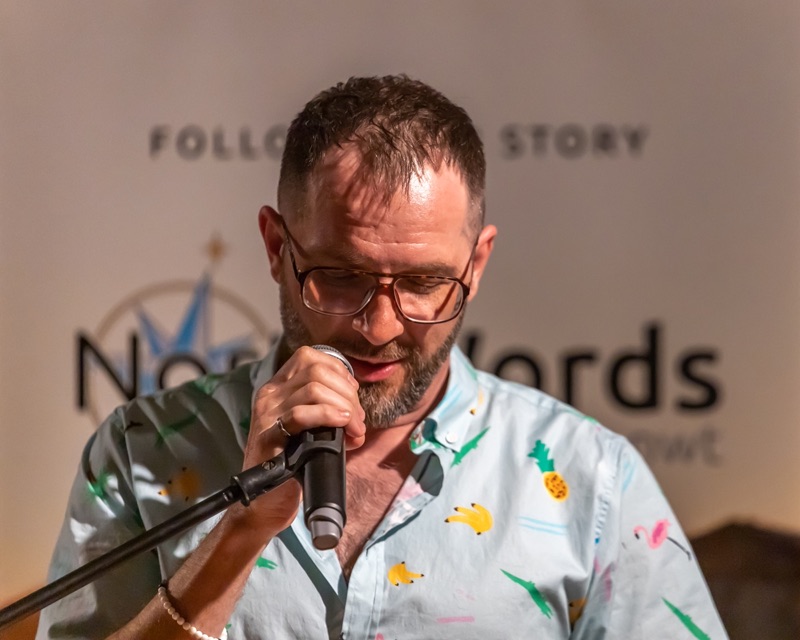 A speaker in glasses and a patterned shirt at the microphone in front of a NorthWords backdrop