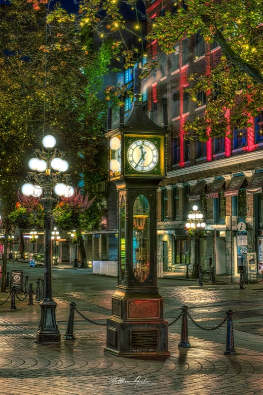 The Gastown steam clock lit at night in Vancouver, street lamps reflected on wet cobblestones