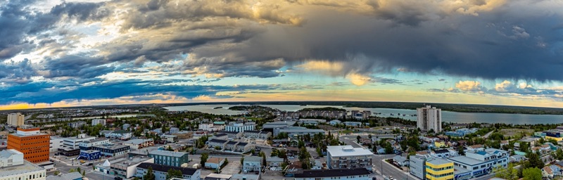 Aerial panorama of Yellowknife beneath dramatic storm cloud, the lake stretching away behind the town