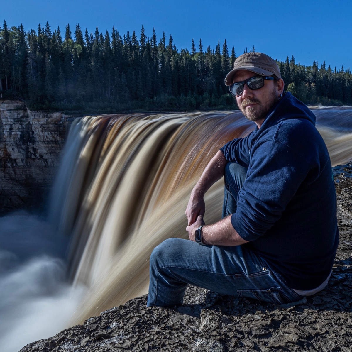Matthew Archer sitting at the lip of a waterfall in the Northwest Territories, the falling water blurred smooth by a long exposure