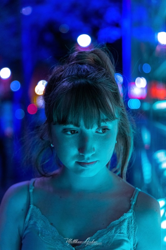 Night portrait of a young woman lit blue by city lights in Montreal, bokeh scattered behind her
