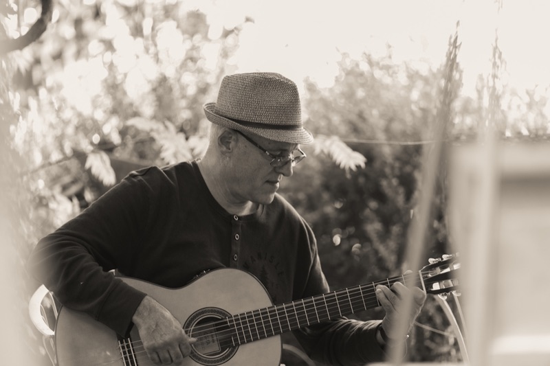 Sepia-toned photograph of a man in a straw fedora playing an acoustic guitar outdoors