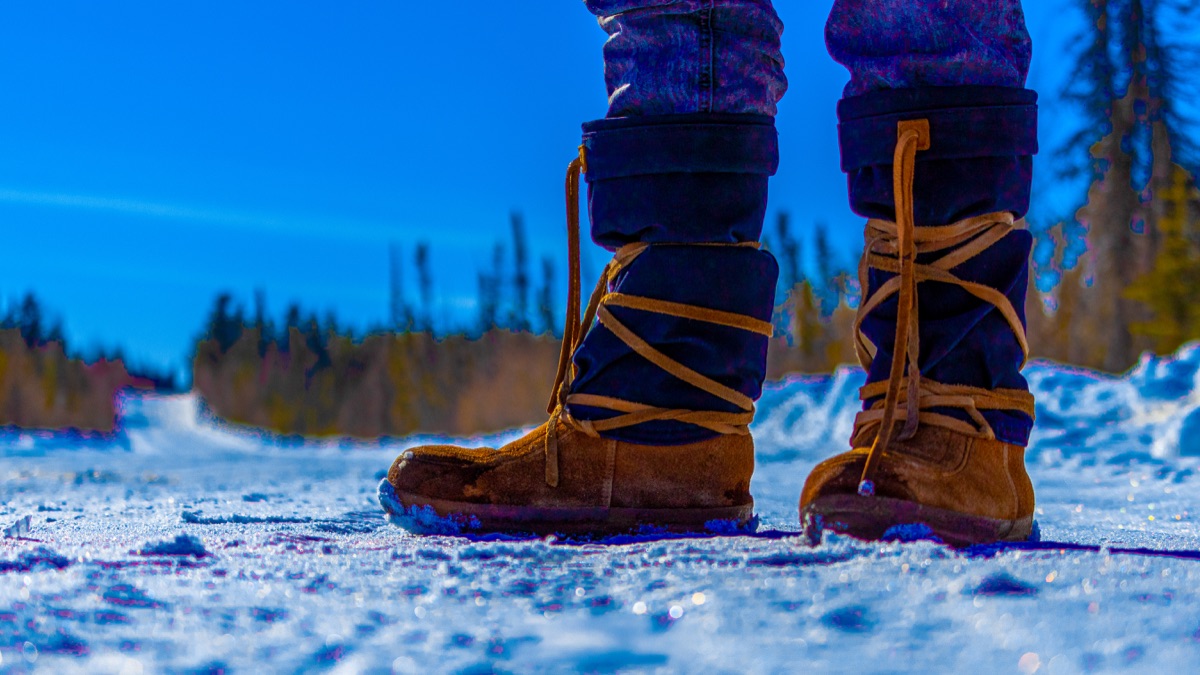Beaded mukluks on a snow-packed road under a hard blue sky — "Mukluks on the Ice Road", a fine art print by Matthew Archer
