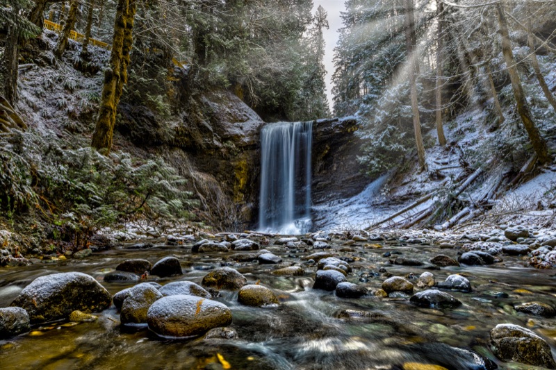 The falls dropping into a snow-dusted canyon, sunbeams through the trees — "Ammonite Falls", a fine art print by Matthew Archer