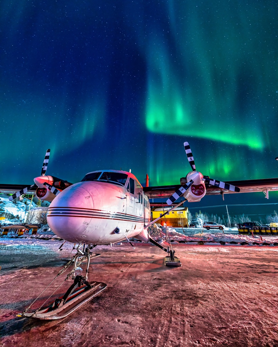A Twin Otter on skis, nose-on and parked for the night, the aurora going off above the apron — "On Call and Standing By", a fine art print by Matthew Archer