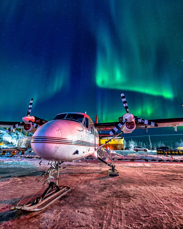 A Twin Otter on skis, nose-on and parked for the night, the aurora going off above the apron — "On Call and Standing By", a fine art print by Matthew Archer